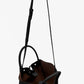 The Proenza Schouler Small Ruched Soft Pebbled Calf Tote is a black leather bucket bag with an adjustable shoulder strap, ruched open top, brown interior lining, and sculptural silhouette, shown against a white background.