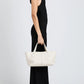 A person in a sleeveless black dress and white shoes stands in profile, holding the Proenza Schouler East West Chelsea Tote with two handles against a plain background.