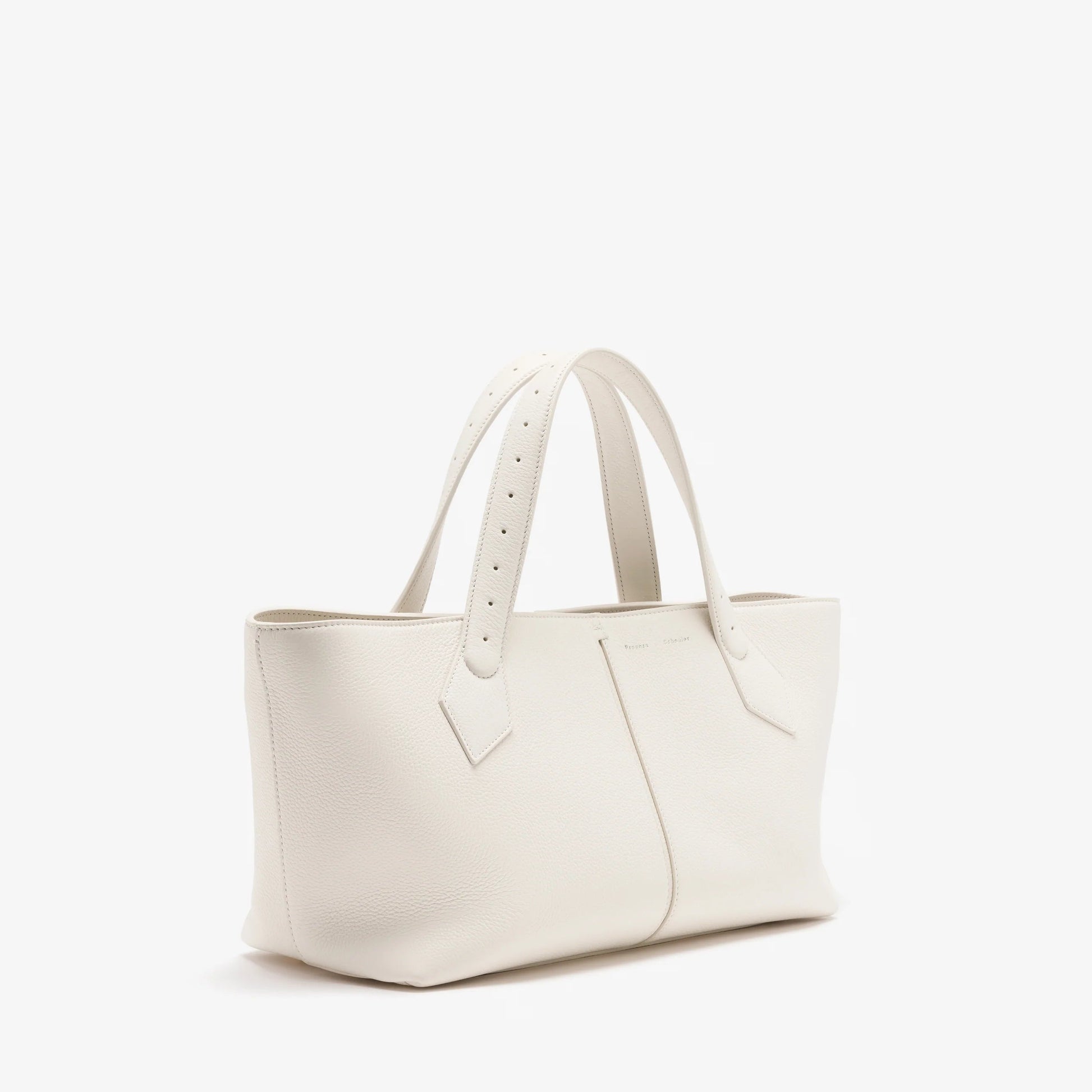 The Proenza Schouler East West Chelsea Tote is crafted from white pebbled calf leather with double handles and a structured silhouette, featuring minimal detailing. Shown against a plain white background.
