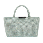 The East West Raffia Chelsea Tote by Proenza Schouler is a light blue woven bag featuring two sturdy handles and a black label at the top center, showcased against a plain white background.