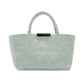 The Proenza Schouler East West Raffia Chelsea Tote is a light blue woven handbag featuring two handles and a small black rectangular accent near the top center. This structured tote is displayed against a plain white background.