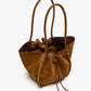 The Proenza Schouler Large Ruched Soft Suede Braided Tote features braided calf handles, a drawstring closure, and an unstructured design, shown here in brown suede on a white background.