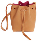 Introducing the Mansur Gavriel Mini Bucket Bag, crafted from exquisite vegetable-tanned leather. This tan bag features a drawstring closure and an adjustable shoulder strap, unveiling a striking red interior.