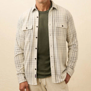 A man wears a Faherty Legend™ Sweater Shirt—a lightweight plaid button-up—over an olive green tee and beige pants, standing against a plain background.
