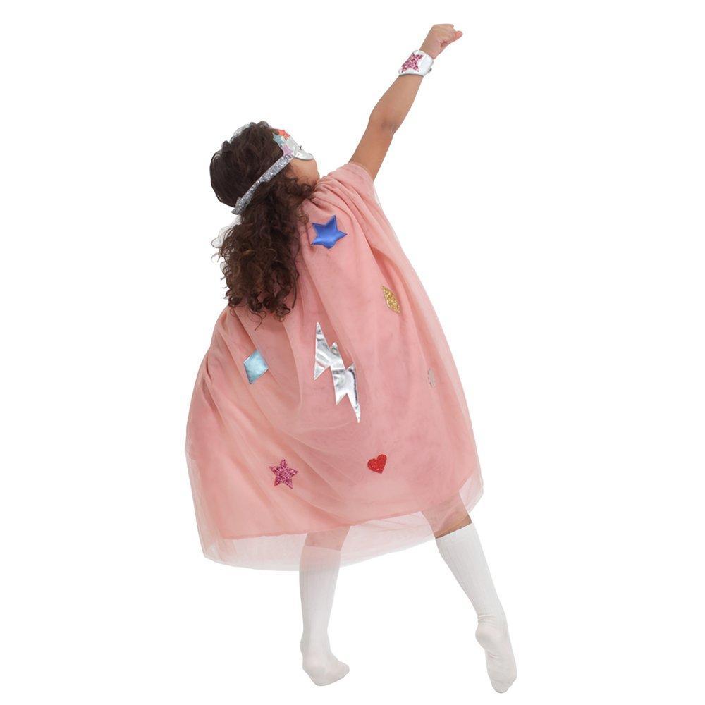 Child wearing the Meri Meri Superhero Dress Up Kit, including a tulle cape, leatherette mask, and wristbands with star motifs strikes a superhero pose, reaching upward with one arm extended.