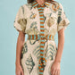 A woman models the Nicole Dress by Hunter Bell NYC—a short-sleeve mini dress with a seashell pattern and vertical orange and teal striped accents—against a light blue background.