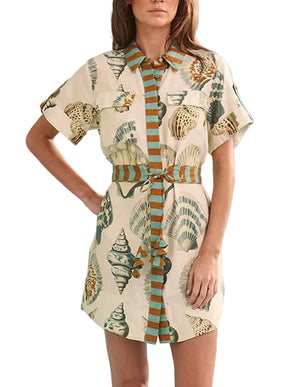 Model wearing the Nicole Dress by Hunter Bell NYC—a collared, short-sleeve shirt dress featuring a seashell print and vertical stripes. Stylish as a chic mini dress or effortless swim coverup.