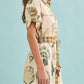 A woman stands against a plain light blue background wearing the Nicole Dress by Hunter Bell NYC, a short-sleeved, belted shirt dress featuring seashell and striped patterns.
