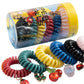 A transparent cylindrical container holds Super Smalls Charmed Life Hair Ties, which come in various colors and are adorned with jeweled charms. Several of these summer accessory hair ties from the Super Smalls brand are also displayed outside the container.