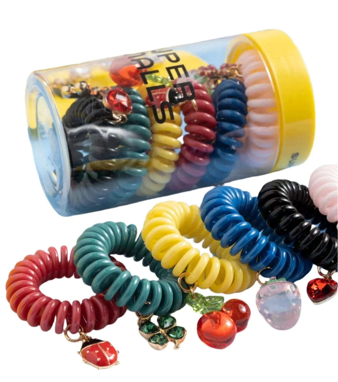 A transparent cylindrical container holds Super Smalls Charmed Life Hair Ties, which come in various colors and are adorned with jeweled charms. Several of these summer accessory hair ties from the Super Smalls brand are also displayed outside the container.