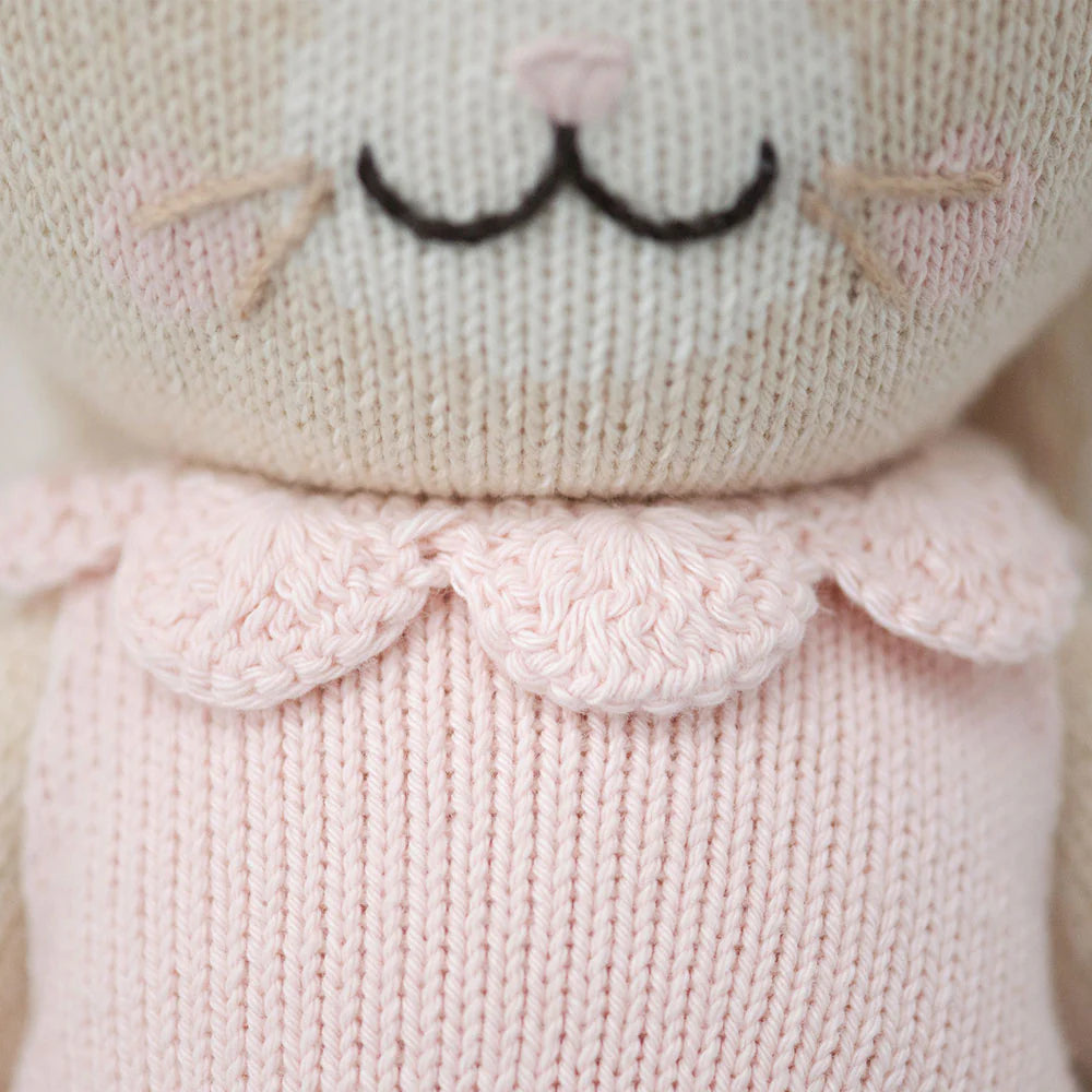 Close-up of Hannah the Bunny - Little 13" by Cuddle + Kind, a knitted stuffed animal in a light pink top with scalloped collar, whiskers, and stitched nose—an adorable inspirational gift for any special occasion.