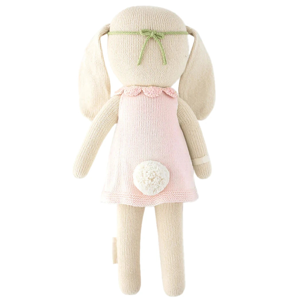 Hannah the Bunny, Blush - Regular 20" by Cuddle + Kind is a knitted plush bunny with long ears, a green headband, pink dress, white tail, and no facial features—perfect as a birthday toy or inspirational gift.