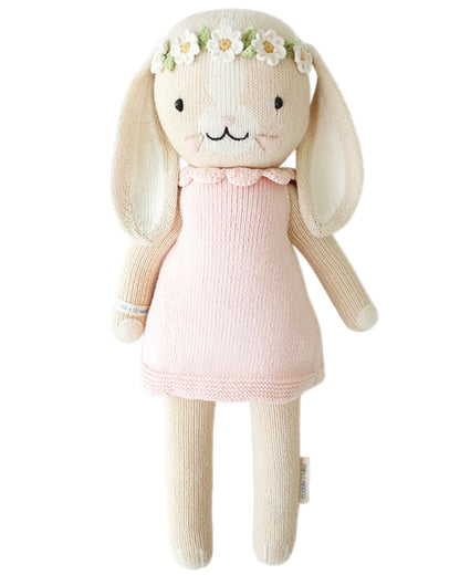Hannah the Bunny - Little 13" by Cuddle + Kind is a knitted bunny doll in a pink dress and flower crown, with long ears and black eyes—a charming birthday stuffed animal or inspirational gift.