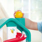 A young child places a yellow ball at the top of the colorful Hape Melody Mansion Ball Run, which features red and green components, indoors.