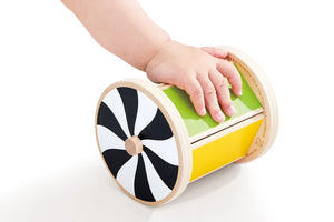 A child’s hand touches the Hape Spinning Drum w/ Mirror, a wooden developmental baby toy featuring a black-and-white spiral design on one end and a green and yellow body, placed on a white surface—perfect for sensory play.