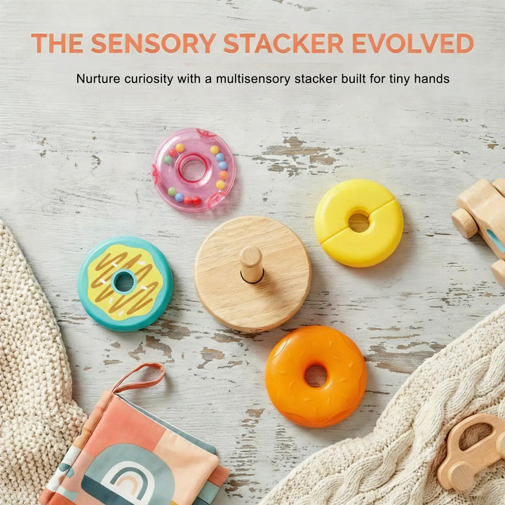 The Hape Stacking Donut Toy features colorful, donut-shaped rings and baby essentials on a light surface; text above highlights this multisensory toy as ideal for encouraging fine motor skills and supporting cognitive development, making it an excellent choice for little hands.