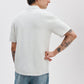 A person faces away from the camera with one hand behind their back, showing tattoos on both arms while wearing the Rag & Bone Harvey Camp Shirt, a retro-inspired white knit with subtle stripes, and light blue jeans.