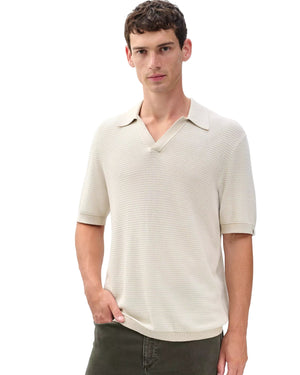 A man wearing the Rag & Bone Harvey Chevron Johnny Polo, a cream-colored lightweight cotton-blend shirt with an open collar, stands with one hand in his pocket against a plain white background.