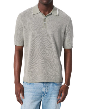 A man wears the Rag & Bone Harvey Knit Polo Shirt in light gray—a vintage-inspired, lightweight cotton blend short-sleeve top—paired with light blue jeans, standing against a white background.