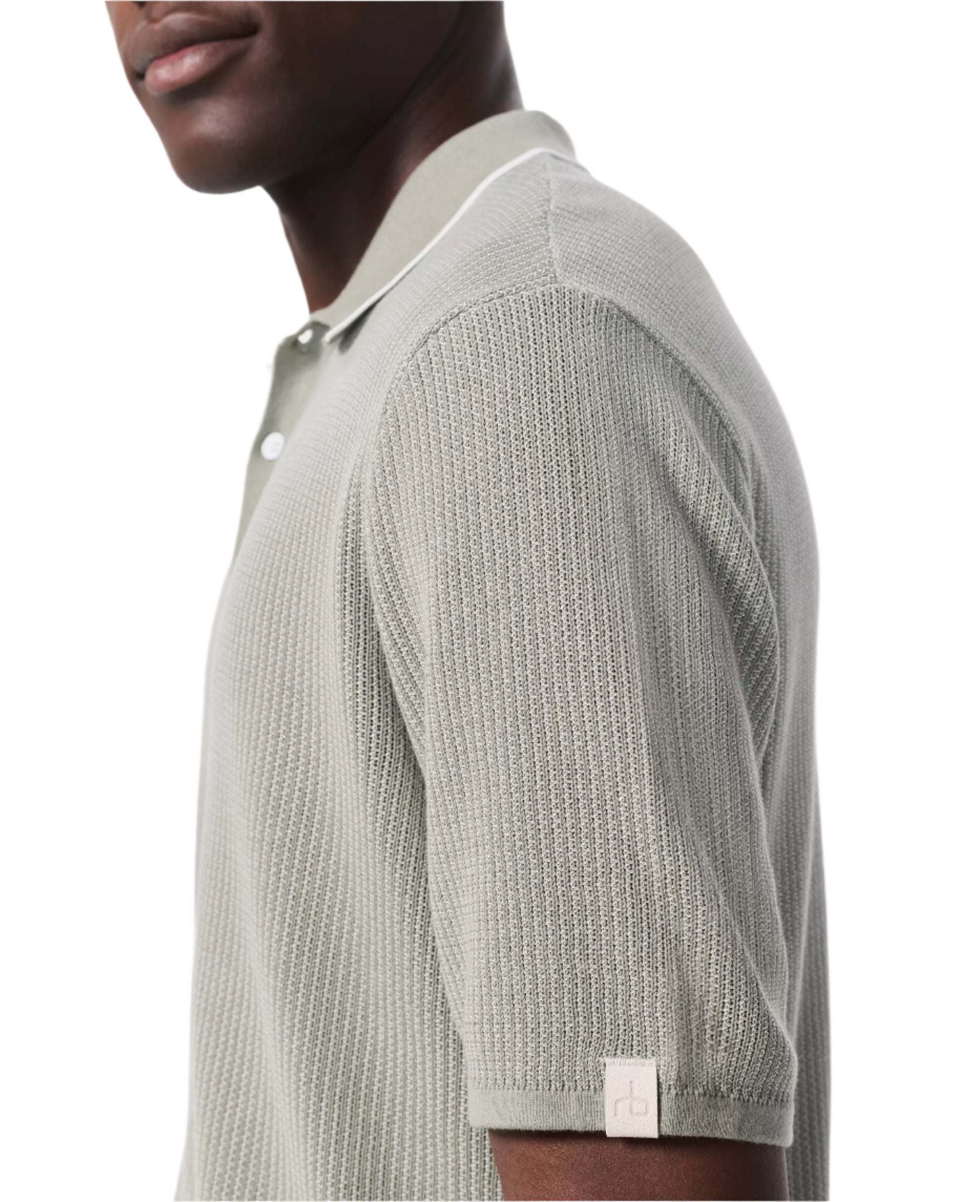 A man wears the Rag & Bone Harvey Knit Polo Shirt in light sage green, a short-sleeve cotton blend polo with a small logo tag on the sleeve cuff.