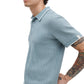 A man models the Rag & Bone Harvey Rib Polo, a light blue patterned cotton-blend short-sleeve shirt, revealing his tattooed right arm against a white backdrop for a subtle vintage feel.
