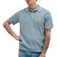 A person wearing the Rag & Bone Harvey Rib Polo—a retro-inspired light blue short-sleeve cotton-blend collared sweater—with jeans, showing tattooed arms.
