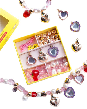 The Super Smalls Make It Heartfelt Mini Bead Kit comes in a yellow organizer box filled with assorted charms, mini beads, and jewelry accessories, displayed alongside finished beaded bracelets and heart-shaped charms.