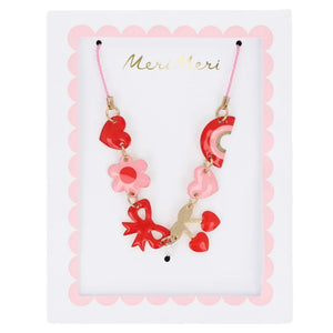 The Meri Meri Hearts & Cherries Enamel Charm Necklace features whimsical red and pink heart, flower, rainbow, and star-shaped enamel charms on a white card labeled "Meri Meri," blending a playful design with a luxurious aesthetic.