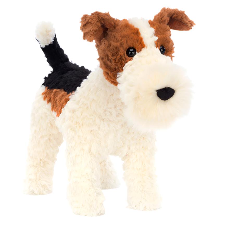 The Jellycat Hector Fox Terrier, a plush toy dog with brown, black, and white fur from the brand Jellycat, stands ready for adventure against a plain background.