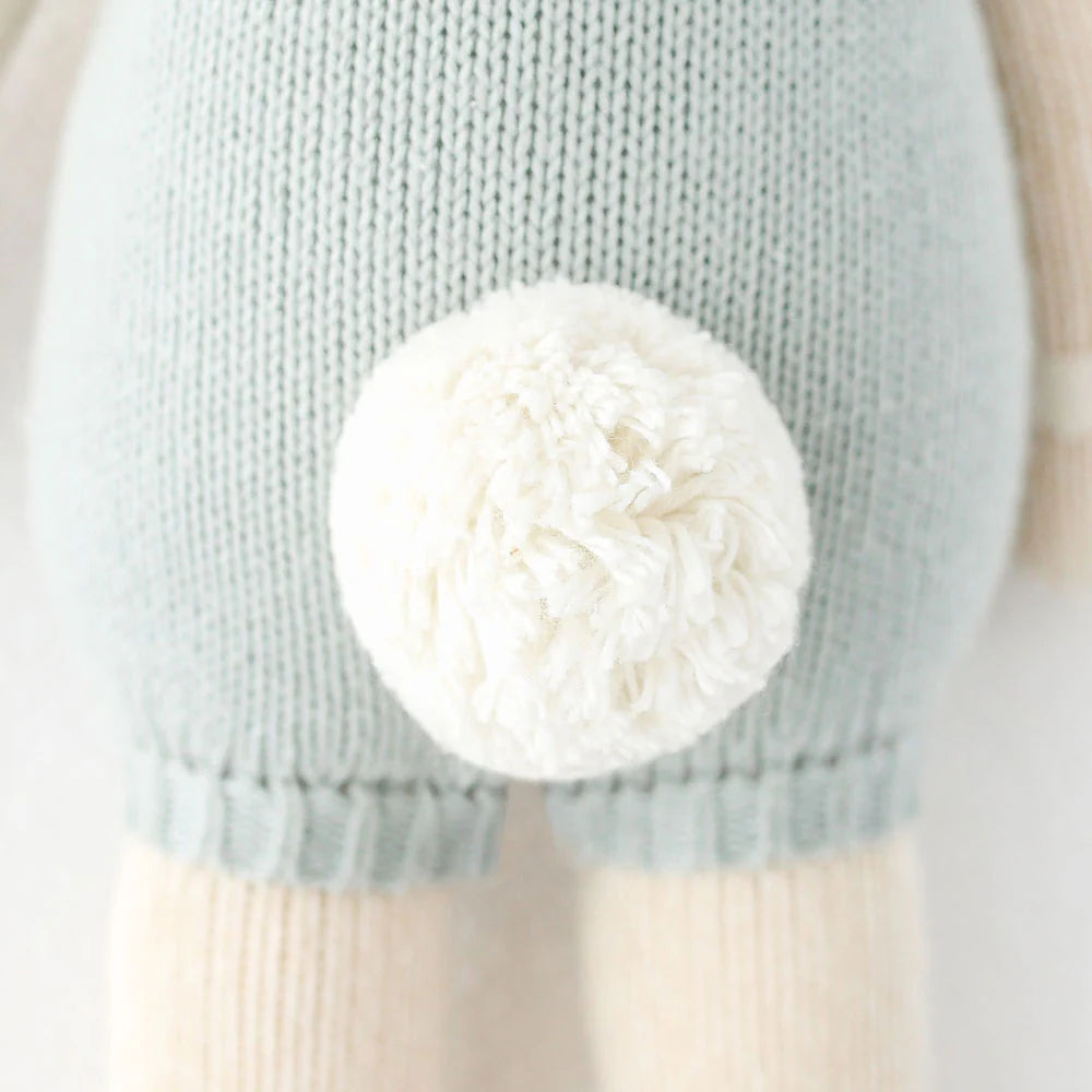 Close-up of Henry the Bunny by Cuddle + Kind, a 20" knitted toy in light blue clothing with a white yarn pom-pom—ready for adventures with best friends.