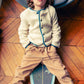 A child with wavy hair sits on a skateboard indoors, leaning back against a chair, wearing the Louis Louise Baby Boys' and Boys' Teddy Bear Fake Fur Jacket in cream with tan pants.