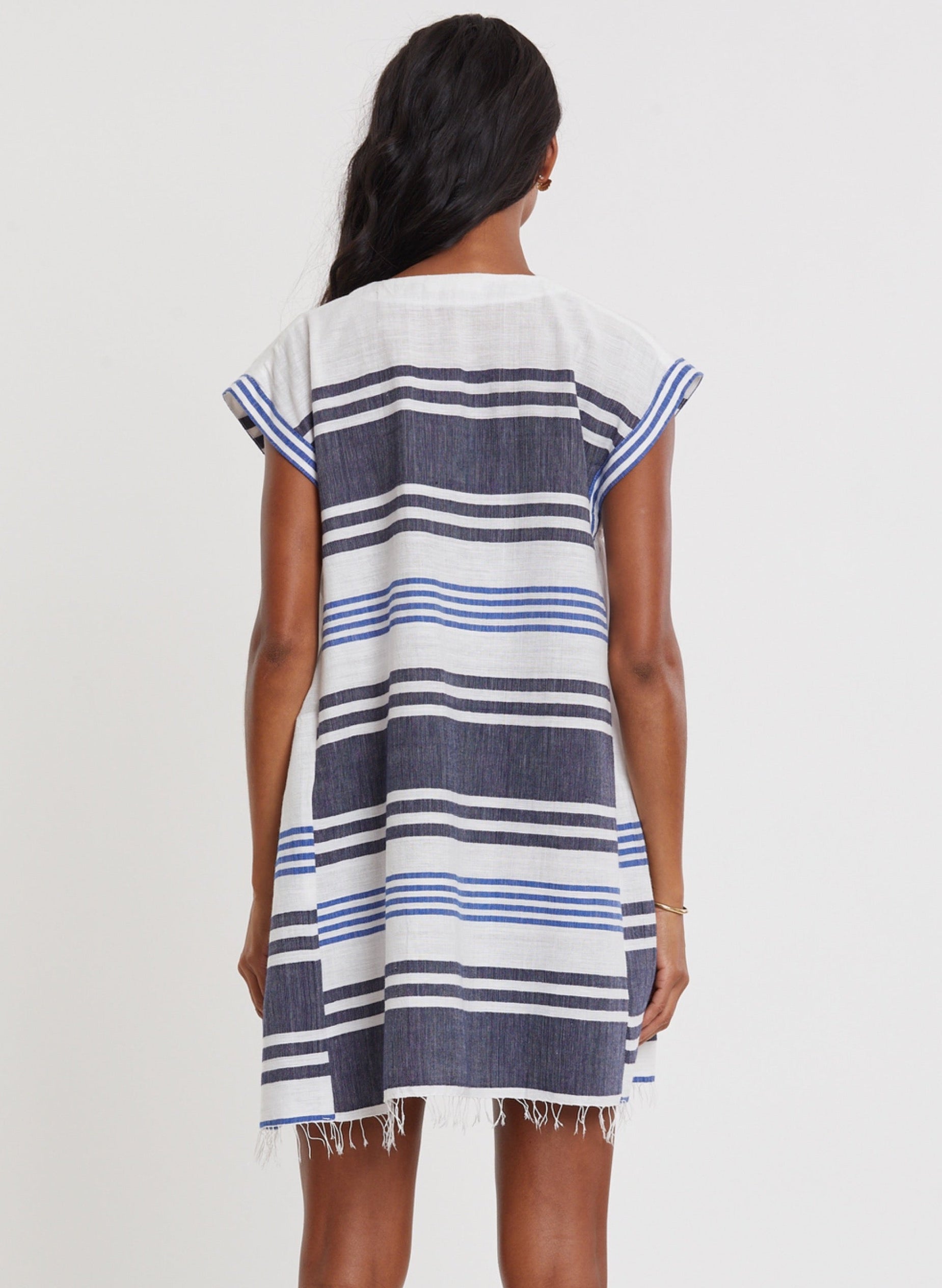 A person with long dark hair is seen from the back wearing the Lemlem Elina Caftan, a short-sleeve, knee-length cotton A-line dress featuring horizontal blue, white, and black stripes.
