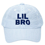 The Lil Bro Baseball Hat by Bits & Bows is a classic light blue and white seersucker cap featuring bold navy “LIL BRO” embroidery on the front.