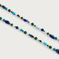 The Milos Beaded Necklace by Anabel Aram features lapis lazuli, turquoise, green, and gold beads arranged on a white background.