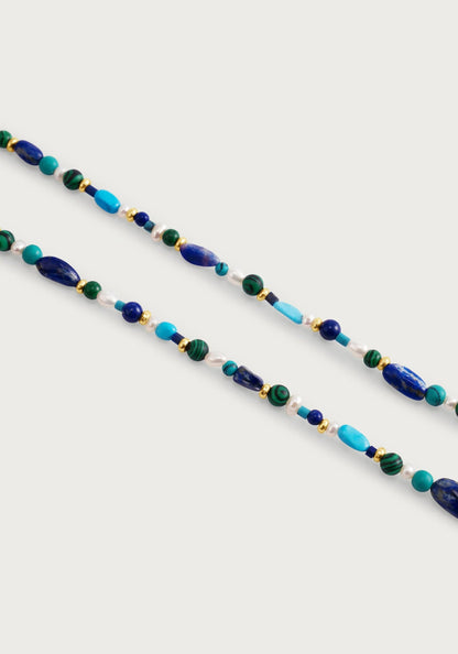 The Milos Beaded Necklace by Anabel Aram features lapis lazuli, turquoise, green, and gold beads arranged on a white background.