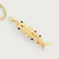The Milos Medium Fish Charm by Anabel Aram is a gold pendant with textured details and colorful gemstone accents, capturing Mediterranean style. Shown on a gold necklace against a light background.