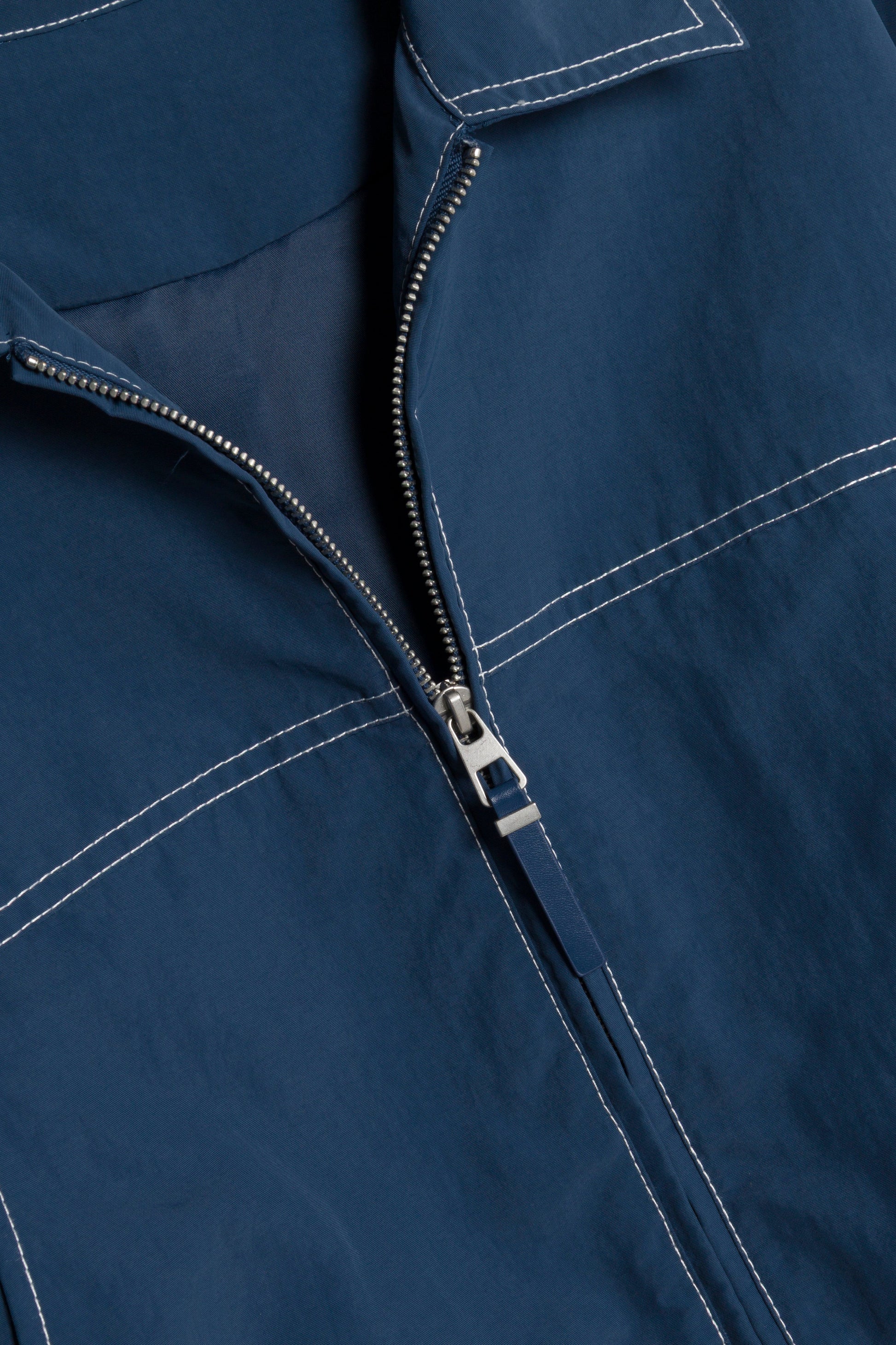 Close-up of the Simkhai Colsen Cotton Cropped Jacket in dark indigo, featuring a silver zipper, boxy silhouette, and white contrast stitching.