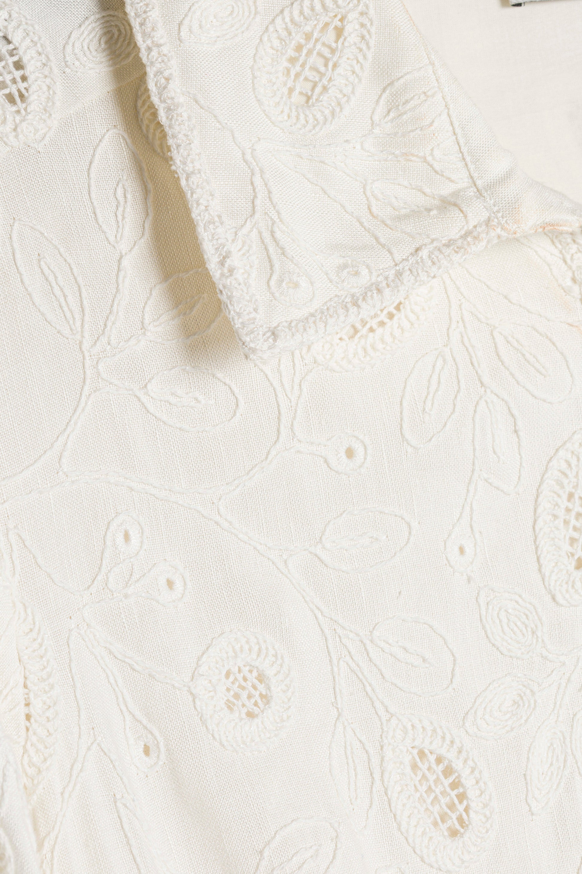 Close-up of the Simkhai Freya Linen Dress, an ivory mini dress in cream linen with intricate embroidered floral and leaf motifs, featuring a collared edge.
