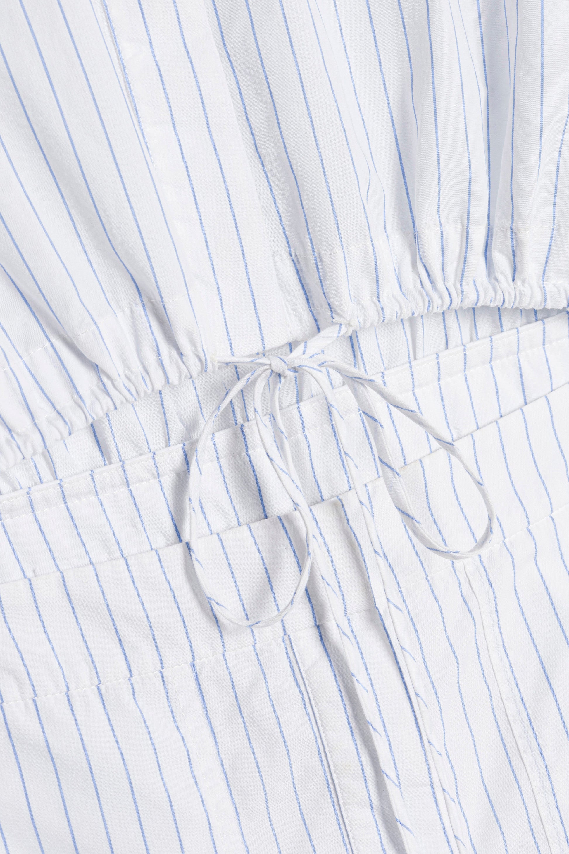 Close-up of the Marcy Cotton Mini Shirt Dress by Simkhai, in white with thin blue stripes and an adjustable drawstring bow at the gathered waist.