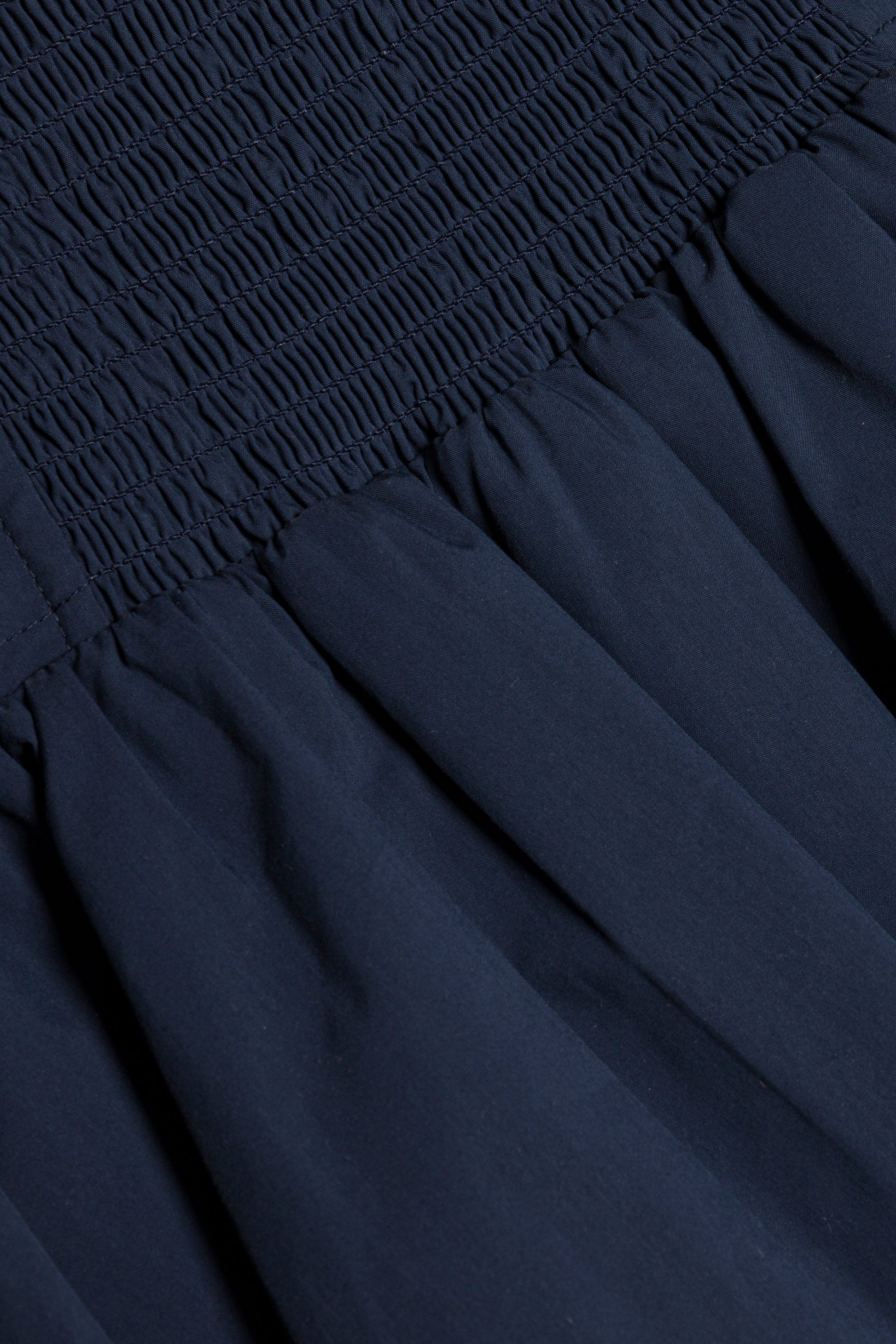 Close-up of the Simkhai Pippa Bubble Mini Skirt in dark blue cotton poplin, featuring a smocked, ruched upper section and a voluminous, pleated lower part.