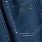 Close-up of a blue fabric pocket with white stitching and a black SIMKHAI label above the pocket, featured on the Lennox Cotton Straight Leg Pant by Simkhai.