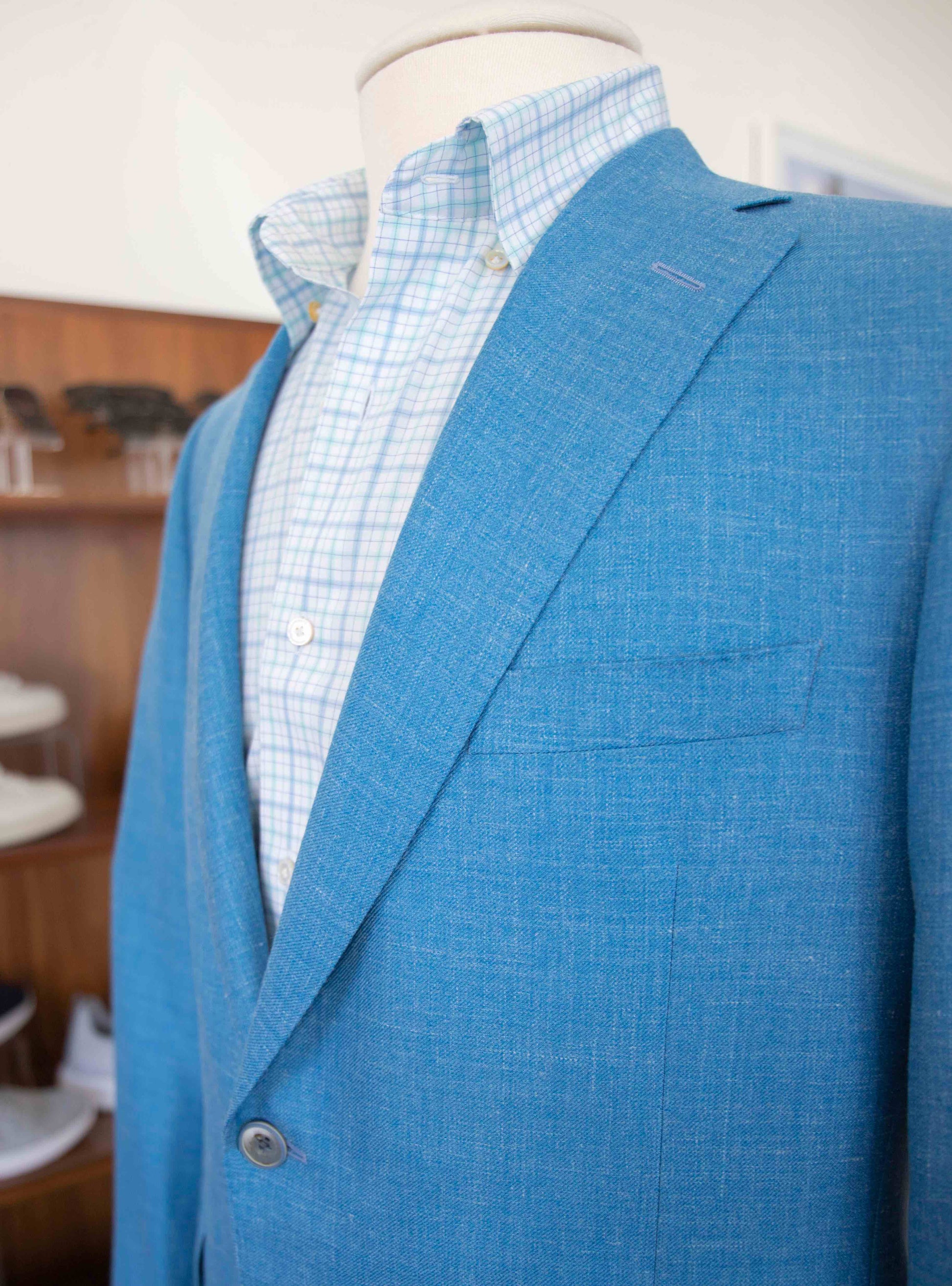 A mannequin wearing a Samuelsohn Bennet Contemporary Fit Blazer over a light blue and white checkered shirt is displayed in a retail setting, showcasing hand-tailored production with exclusive fabrics.