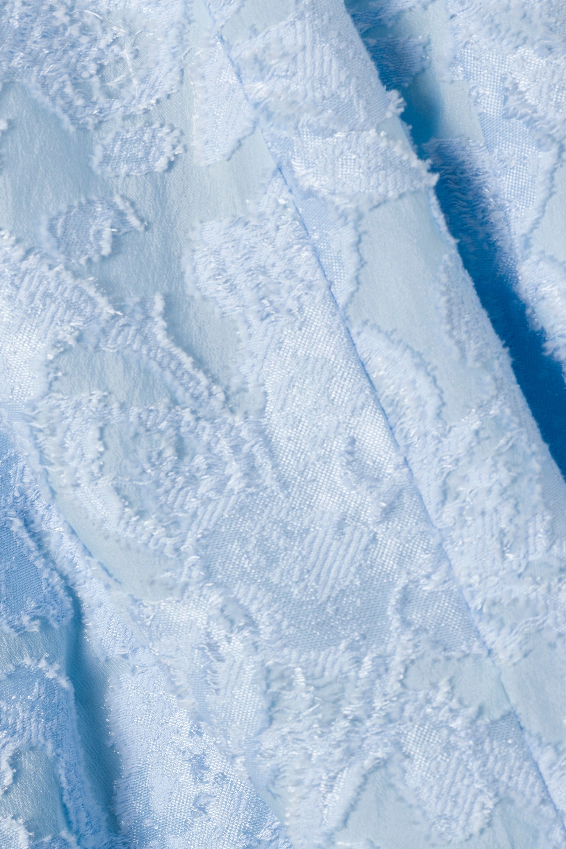 Close-up of the Valeria Jacquard Dress by Simkhai, featuring light blue textured fabric with a raised floral jacquard pattern—perfect for an elegant look.