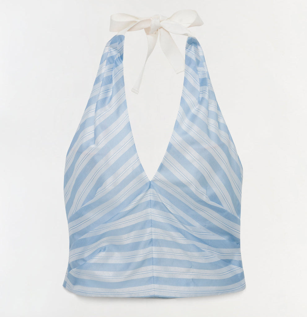 The Caprie Halter Top by Simkhai features light blue and white stripes in soft yarn-dyed satin, a deep V-neck, and a white ribbon neck tie, shown against a plain white background.