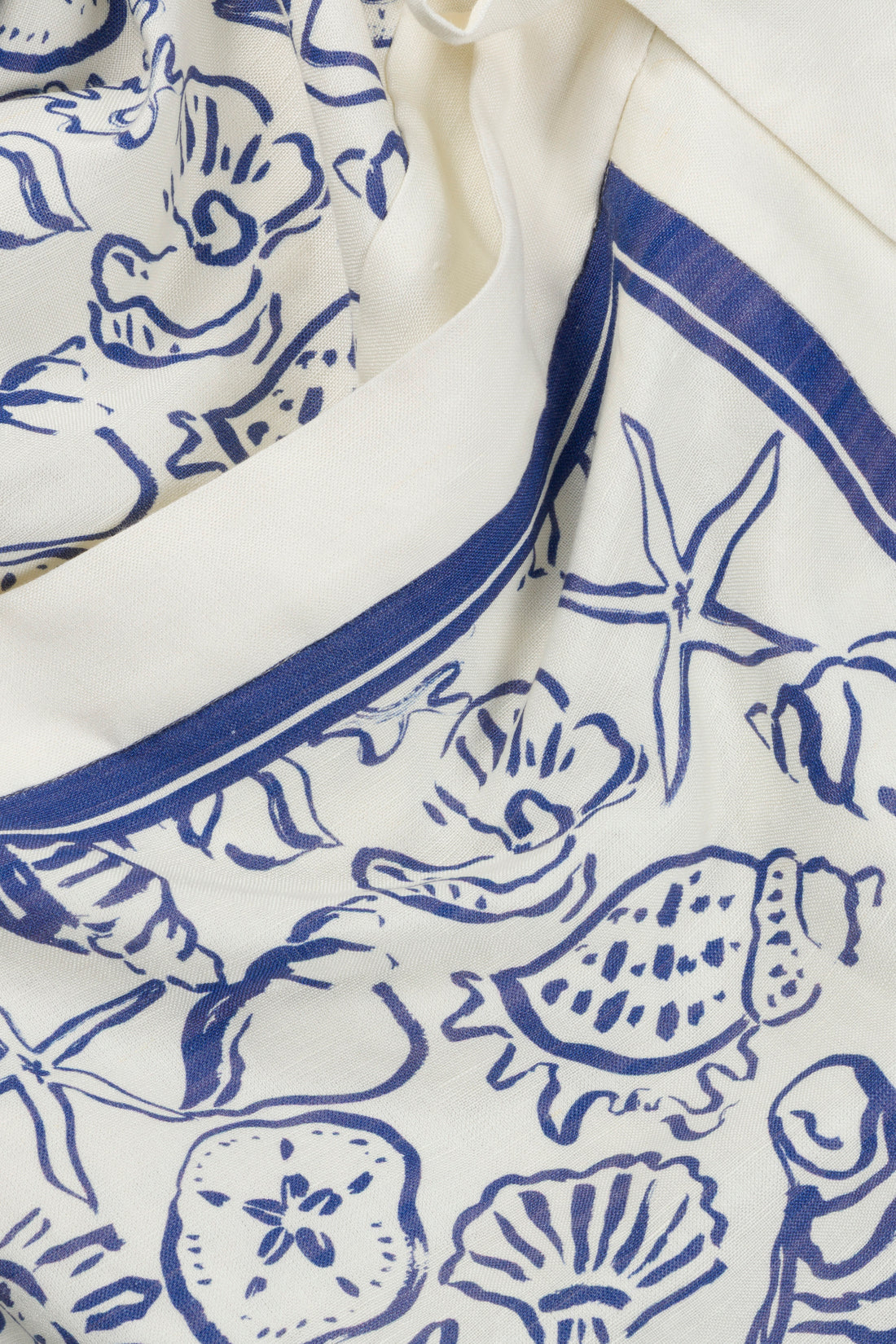 Close-up of cream-colored fabric with blue seashell, starfish, and marine motif line drawings, finished with a blue border—perfect for the Darbie Linen Mini Dress by Simkhai.
