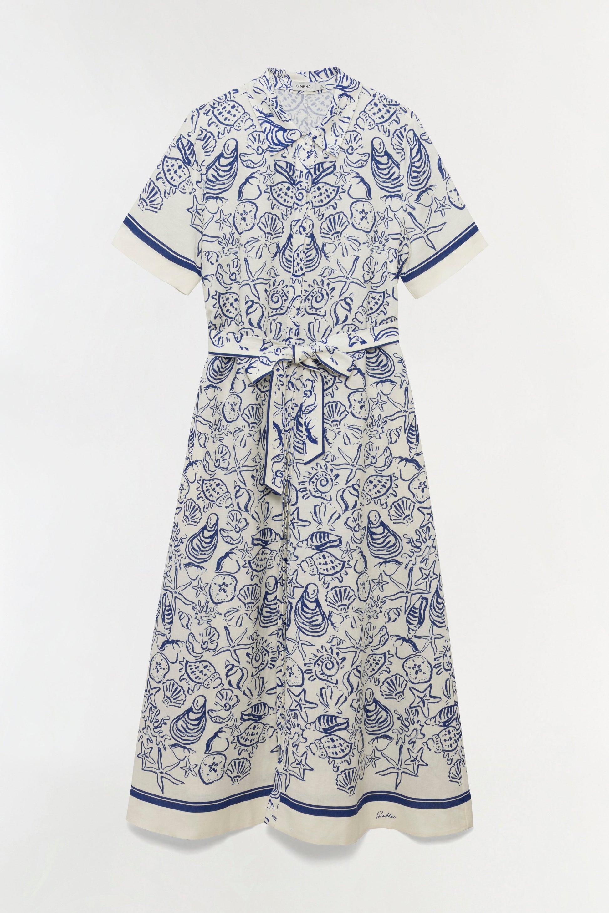 The Simkhai Audria Linen Midi Dress features a white short-sleeve design with a belted waist and blue marine-inspired seashell and starfish print, shown on a plain background.