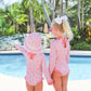 Two young girls in The Beaufort Bonnet Company's Sarasota Surf Suits stand by the pool, surrounded by palm trees—a sunny day with perfect sun protection for their adventures.