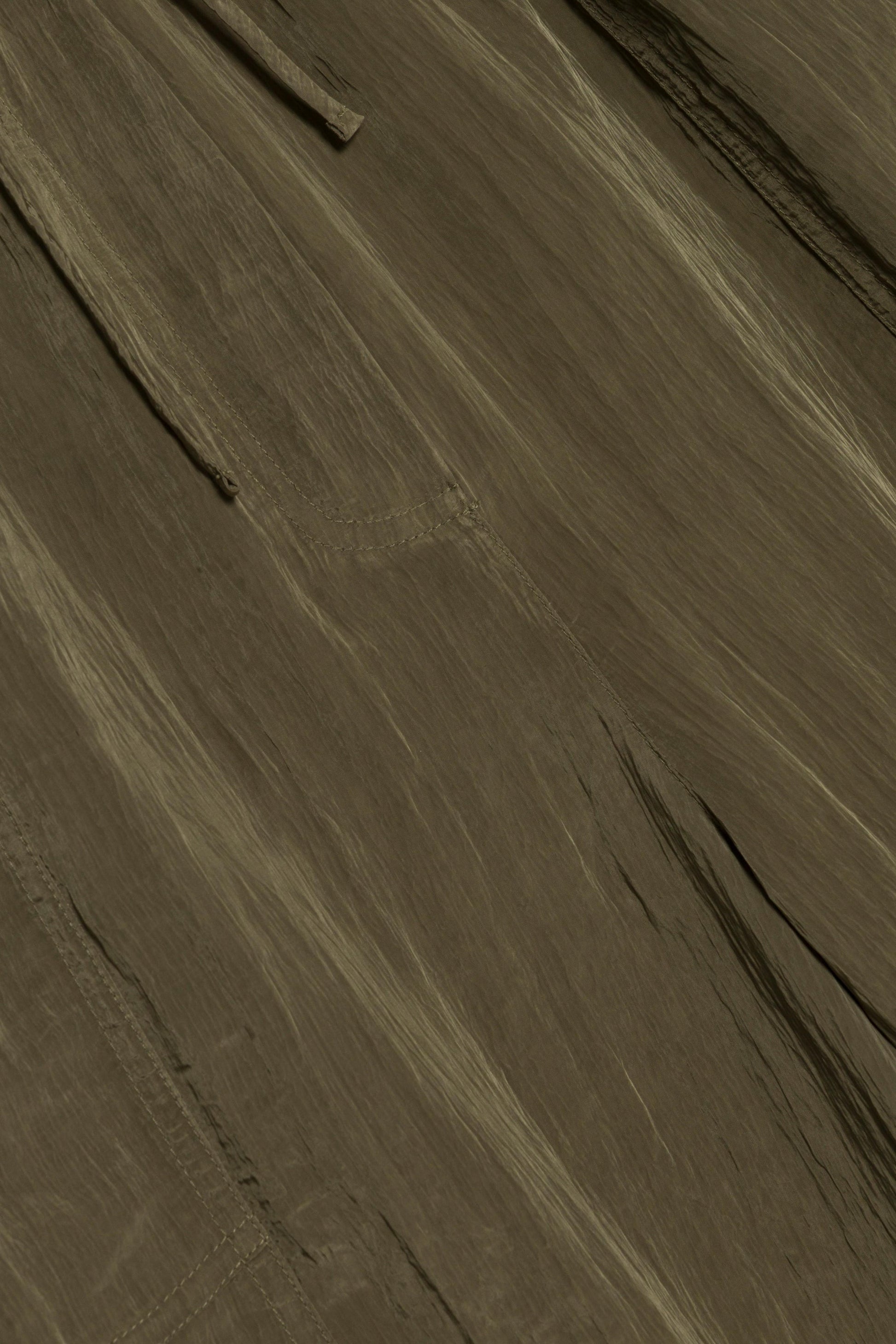 Close-up of Simkhai's Freya Parachute Pant fabric, showcasing visible seams and a textured, slightly wrinkled brown surface.
