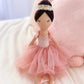 The Juliet Prima Ballerina Doll from Mon Ami, dressed in a pink tulle dress and floral headband, elegantly sits on a plush pink pillow, ideal for imaginative play.