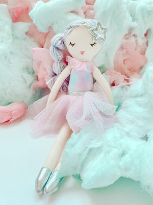 The MON AMI Sachet Scented Doll by Mon Ami features braided pastel hair, a star headband, a pink tutu, and silver shoes, all while sitting on a bed of colorful cotton-like material. This delightful fabric doll carries a sugary scent that makes it even more charming.